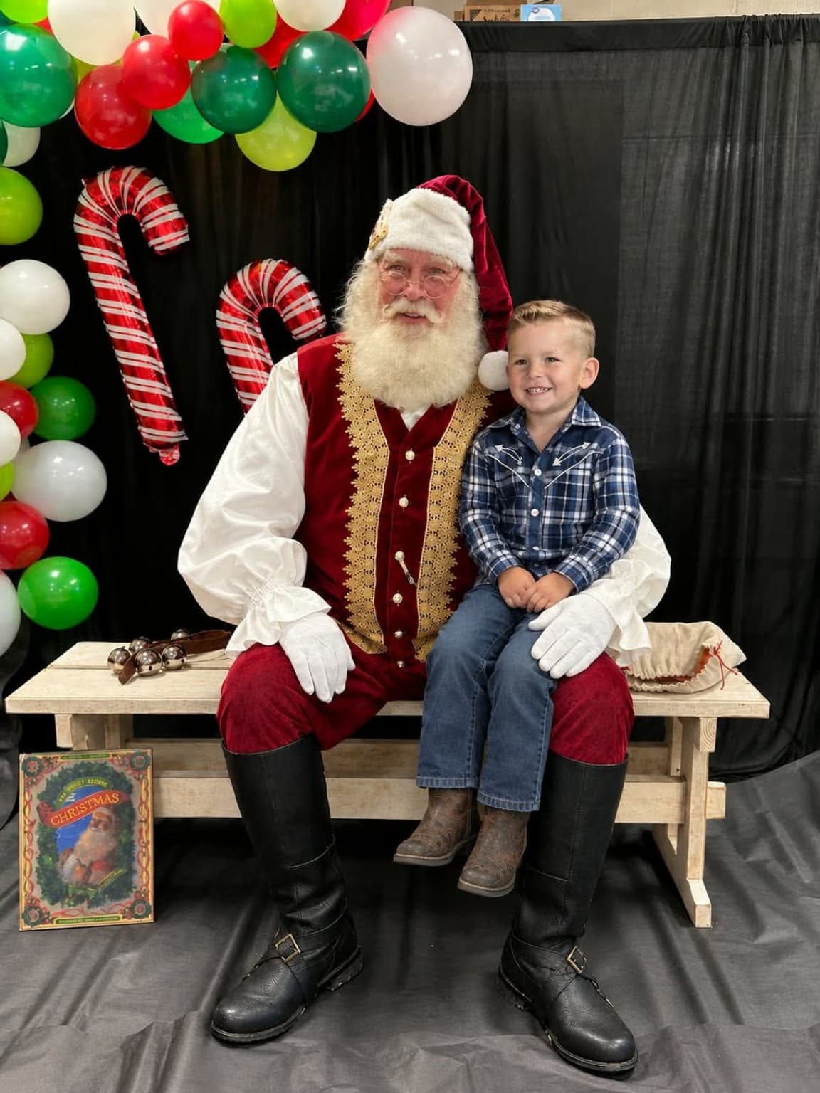 Santa Steve Rowlett, a real-bearded Santa in traditional attire, sharing a warm Christmas moment with a young visitor.